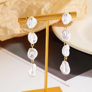 Detail of long drop baroque pearl earrings with gold chain on a jewelry display stand