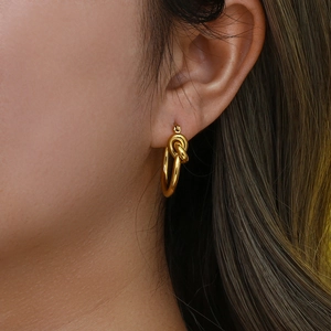 Golden titanium steel knotted hoop earrings shown as worn on a female model