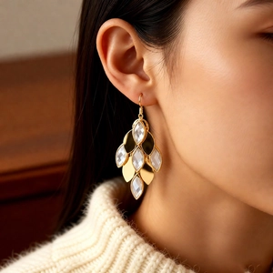 Detail view of gold-plated teardrop earrings with white translucent gems on a female model