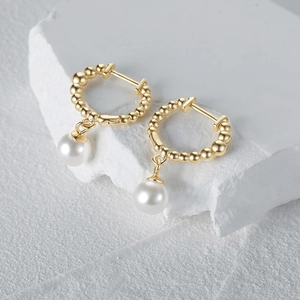 Macro detail of elegant S925 silver gold beaded hoop earrings with white hanging pearls