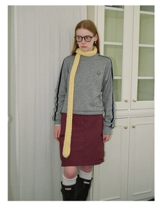 Detail of a long pale yellow chunky knit scarf paired with a retro sports outfit