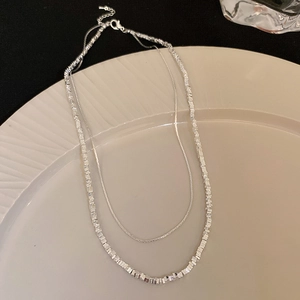 Close-up of double-layered silver necklace with square beads and snake chain on a white plate