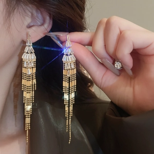 Close-up of golden tassel earrings with sparkling tiered zircon stones worn by a model