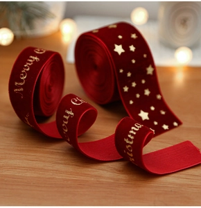 Macro detail of red velvet Christmas ribbon with gold Merry Christmas print on wood