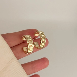 Close-up of gold chain link hoop earrings with textured metal finish held by a model