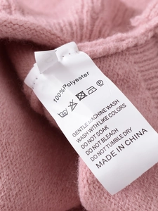 Detail view of pink knit sweater care label showing 100 percent polyester fabric and size S