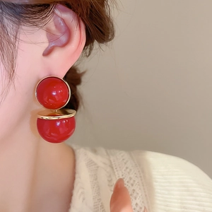 Gros plan de boucles d'oreilles perles rouges et dorées portées par un modèle