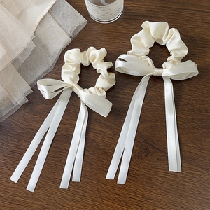 Detail of cream silk satin scrunchies with elegant long ribbons on a wood surface