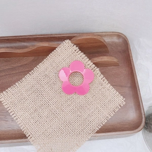 Detail view of a pink flower hair clip resting on linen fabric with a wooden tray