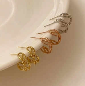 Close-up of gold and silver twisted rope stud earrings on a white ceramic plate