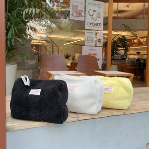 Lambswool makeup bags in black, white, and yellow colors on a wooden windowsill