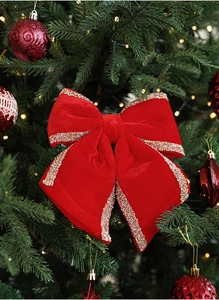 Close-up of red velvet Christmas bow with gold glitter edges hanging on a tree