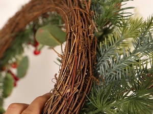 Close-up of Christmas wreath with natural rattan base, pine needles and red berries