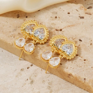 Detail of gold zircon earrings with heart and teardrop stones on stone background