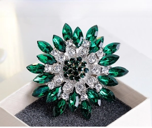 Detailed macro view of a sun-shaped brooch with emerald green marquise cut crystals