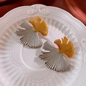 Two-tone ginkgo leaf stainless steel earrings with textured veins on white porcelain