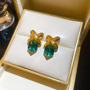Macro shot of gold-plated crossover stud earrings with green square crystals in a jewelry box
