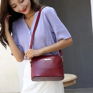 Detail view of burgundy pebble leather shell bag with gold logo on model's shoulder