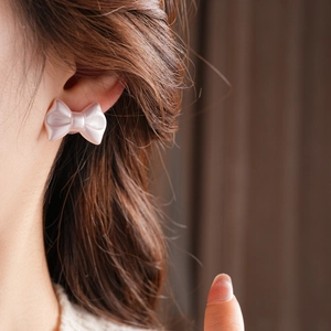 Close-up of pink satin bow earrings with pearlescent finish worn by a model