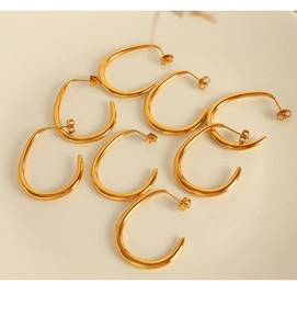 Macro shot of multiple high-polish gold U-shaped earrings on a warm ceramic surface