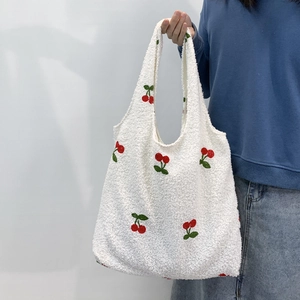 Close-up of white fleece tote bag featuring red cherry embroidery detail with soft texture