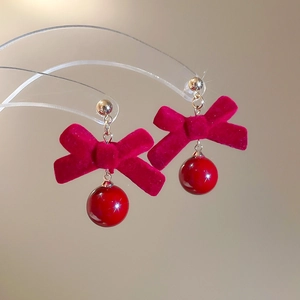 Détail de boucles d'oreilles nœud en velours rouge avec perles et finitions dorées