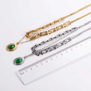 Detail of layered gold and silver chains with emerald green stone pendants and scale
