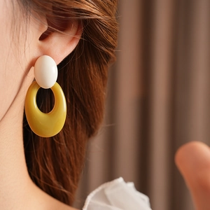 Close-up of model wearing geometric resin oval drop earrings in white and yellow-green