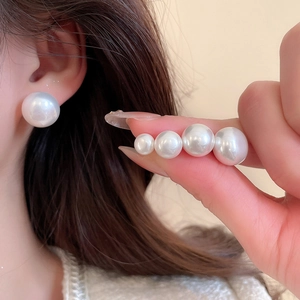 Macro shot showing four different sizes of elegant white round pearl earrings on model