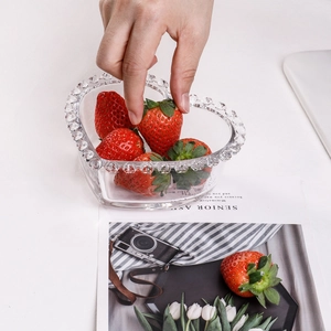 Heart-shaped glass bowl with beaded rim holding fresh strawberries in a lifestyle setting