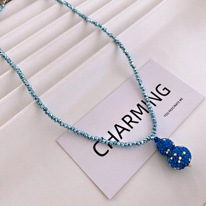 Macro detail of a blue beaded necklace featuring a sparkling crystal pave gourd pendant