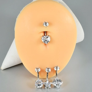 Detailed view of heart, star, and square zircon navel rings on a silicone body model