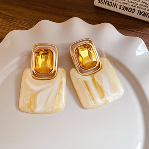 Detail of vintage gold earrings with yellow crystals and marble texture resin pendants