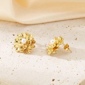 Macro shot of gold floral earrings with white pearls on a textured background