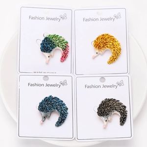 Detailed view of hedgehog brooches in four colors on display cards in a white ceramic dish