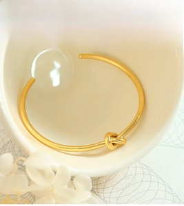 Detailed view of elegant gold-toned knotted open bangle placed in a ceramic bowl