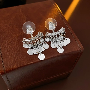 Close-up of silver tassel earrings with round sequins on a brown leather jewelry box
