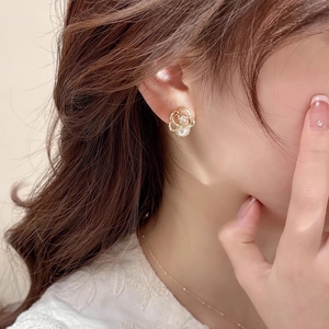 Detailed close-up of a gold rose stud earring with a white pearl on a model ear