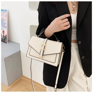 Detail of a chic cream-white crossbody bag with gold-tone buckle on a black suit model