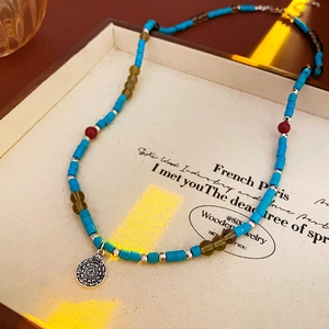 Macro shot of ethnic beaded necklace with blue cylinders and engraved silver pendant