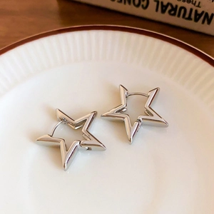Close-up of star-shaped silver hoop earrings placed on a white ceramic tray with red rim