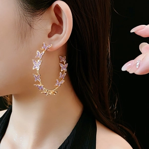Gros plan de boucles d'oreilles créoles dorées avec papillons mauves sur modèle