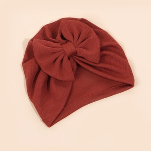Détail d'un bonnet de bébé en maille côtelée rouge brique avec un grand nœud