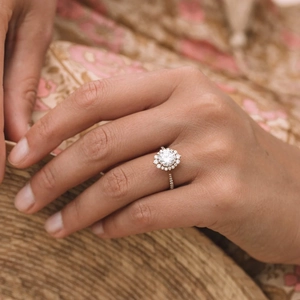 Elegant gold flower halo ring with cubic zirconia worn by model in soft natural light