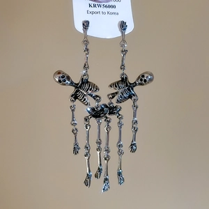 Close-up of gothic silver skull tassel earrings with movable joint chains on display card