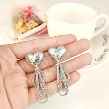 Detail showing silver heart tassel earrings with sparkling rhinestones and wave fringe