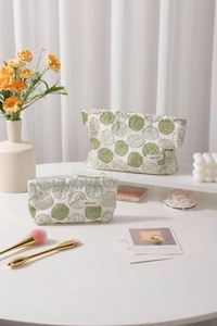 Close-up of cotton linen makeup bag with green floral embroidery and plush pom-poms