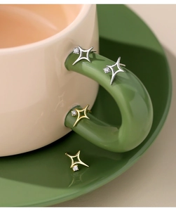 Detail of hollow S925 silver North Star earrings with zircons on a coffee cup handle