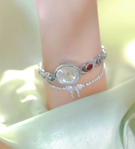 Silver watch with red and purple gemstones on wrist over green silk fabric detail