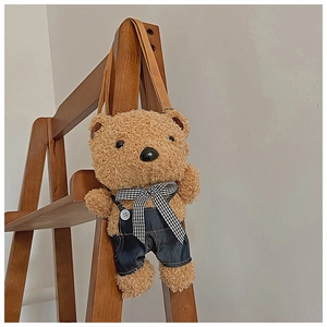 Detail of brown plush teddy bear crossbody bag in denim overalls hanging on wooden rack